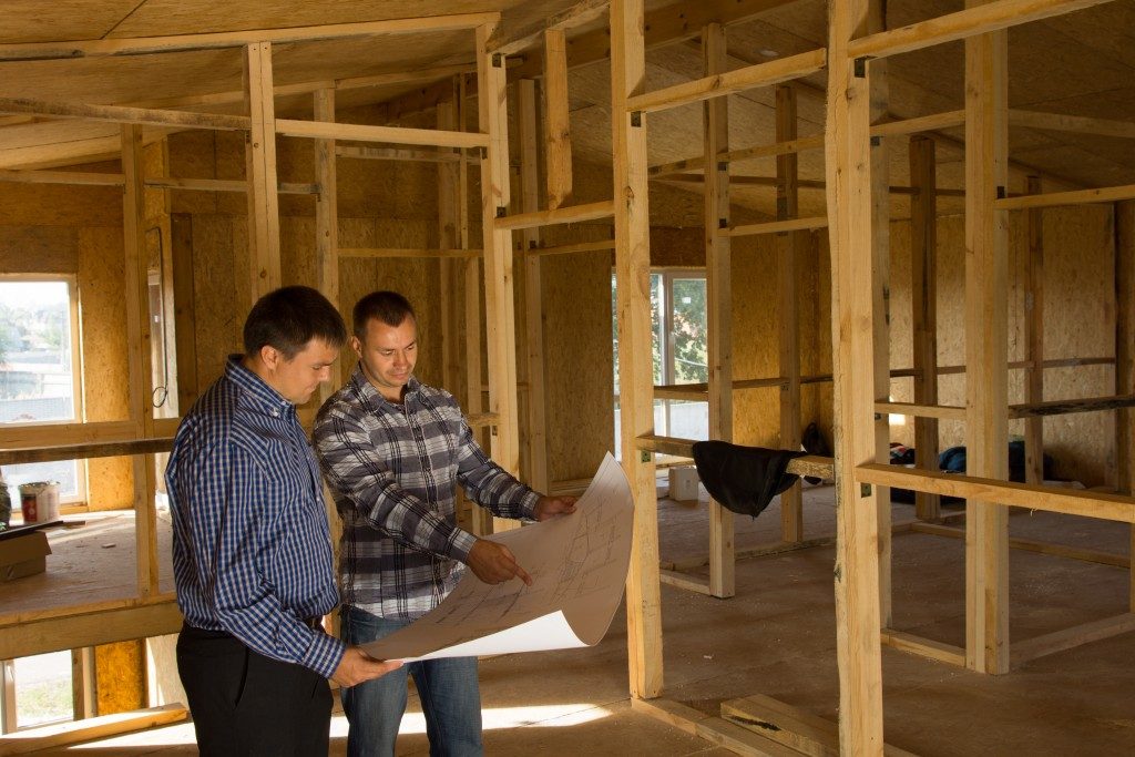 Two builders standing with an open blueprint discussing the interior of a custom home