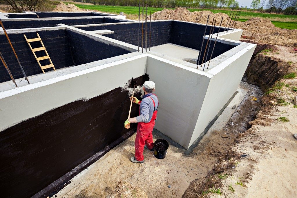 Man waterproofing foundation of building