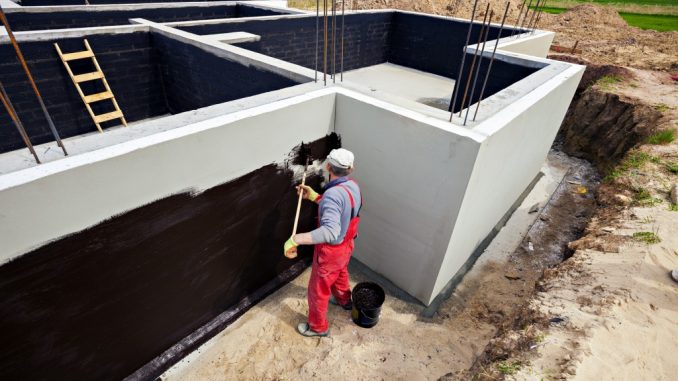 Man waterproofing foundation of building
